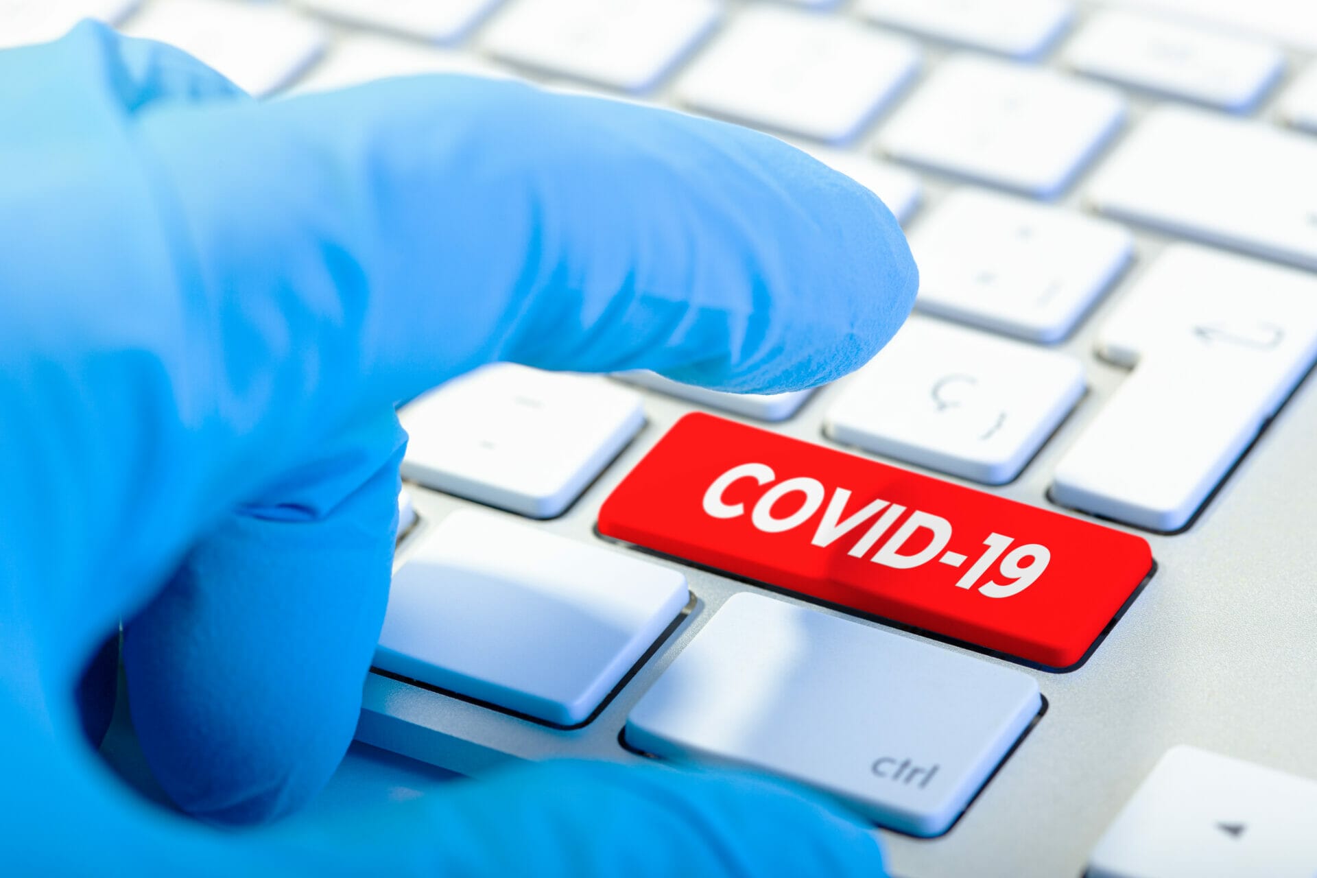 Hand with protecting glove and Keyboard with red key and COVID-19 message. Coronavirus concept Die Massnahme die so gut wirkt, dass sie bereits vor Einführung Resultate bringt